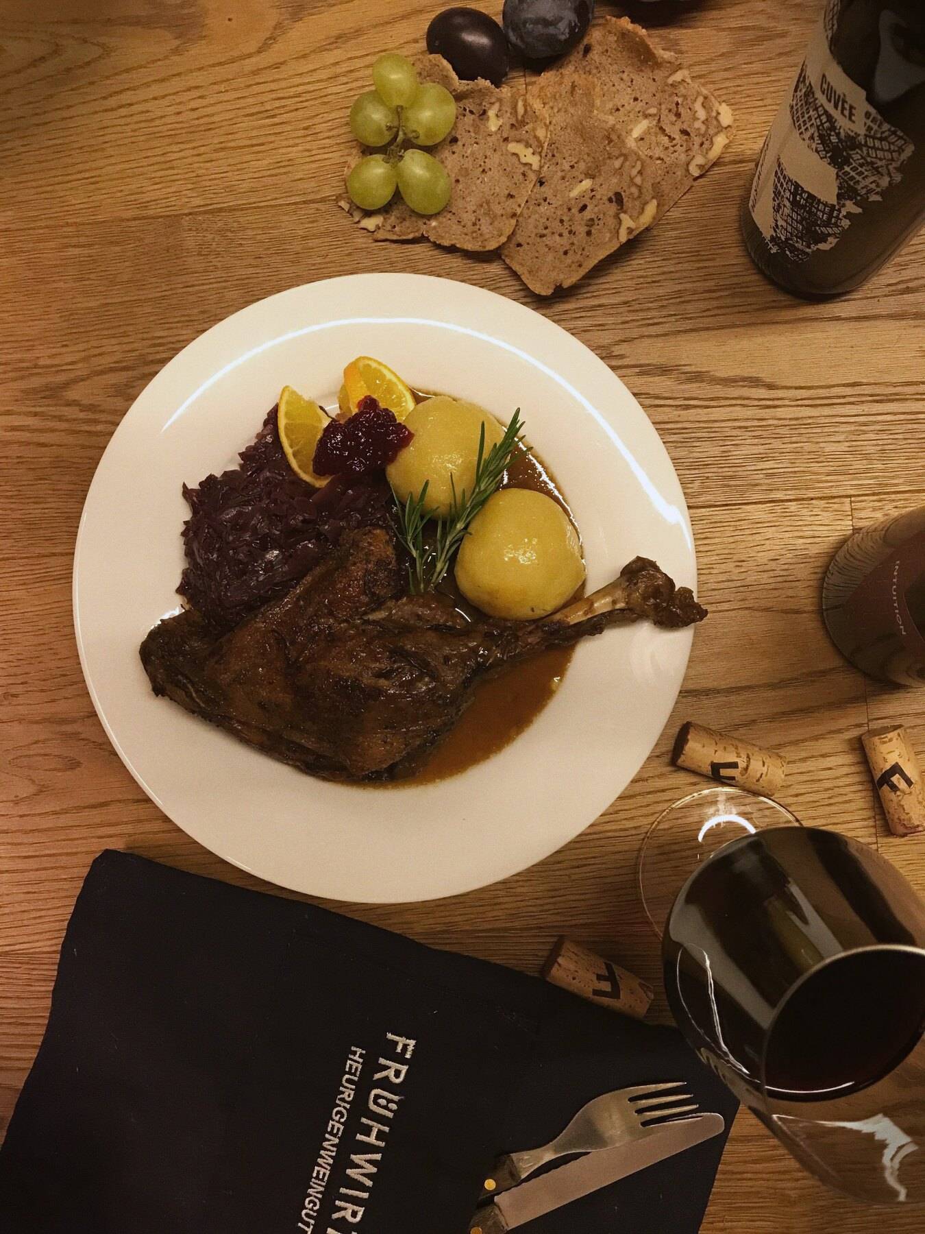 Knusprig gebratenes Gansl (ein Viertel) mit Erdäpfelknödel, Rotkraut, Orange und Preiselbeeren von oben, daneben ein Glas Rotwein