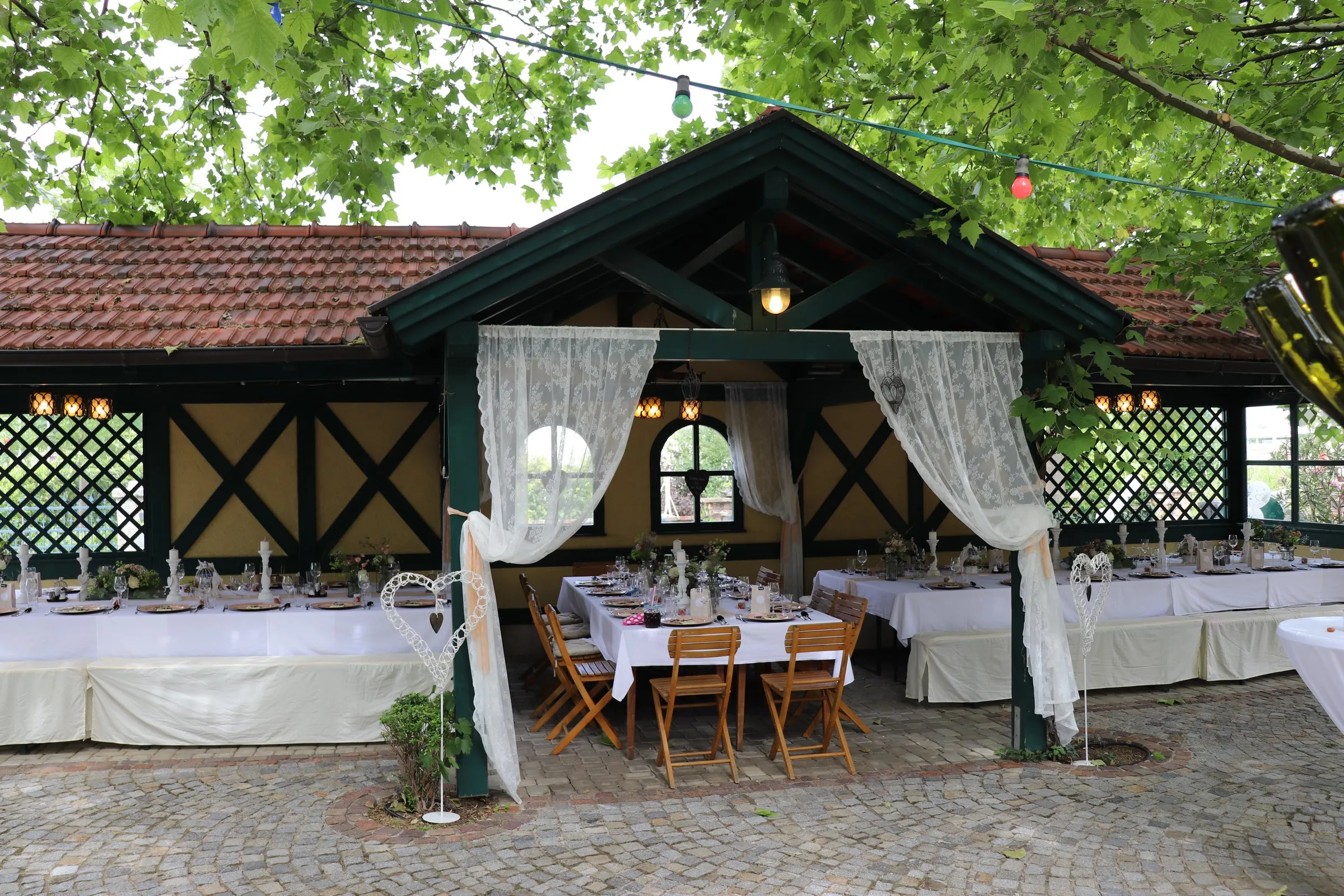 Das Salettl unter Platanen, festlich gedeckte lange Tafeln mit weißen Tischtüchern, Kerzen und Blumen, Lichterkette darüber
